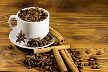 Coffee beans in white cup, cinnamon sticks and star anise on wooden table