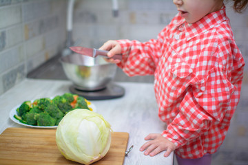 cute baby weighs buckwheat and vegetables on kitchen scales. A little girl is cooking vegetarian...