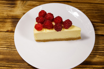 Piece of tasty New York cheesecake with raspberries in a white plate on wooden table