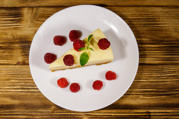 Piece of tasty New York cheesecake with raspberries in a white plate on wooden table. Top view