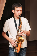 Fototapeta premium A boy of teenage age plays a saxophone at home and prepares for a performance on a big stage
