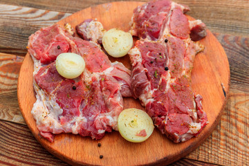 Fresh raw pork meat with spices and onion on wooden cutting board on rustic table