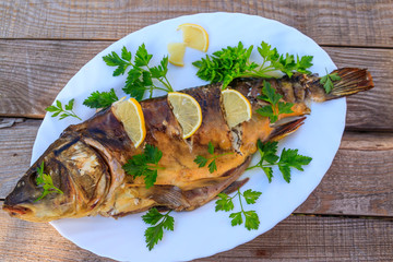 Baked carp fish with lemon and parsley on wooden table