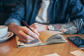 Man hand with pen writing on notebook on a wooden table. Close-up