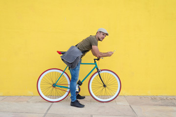 Young man leaning on bicycle, using smart phone
