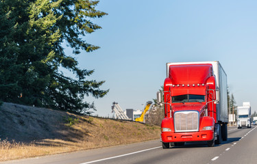 Fototapeta na wymiar Big rig bright red classic American idol semi truck with reefer semi trailer driving on the straight highway in sunny day
