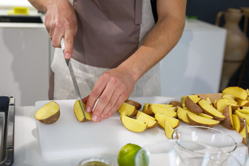 Chef cutting potatoes wedges on white table. Culinary master class on light kitchen