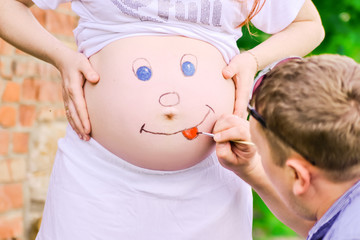 Happy smiley face painting on the belly of pregnant woman. Concept about love and happiness