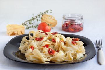 Fettuccine pasta with sun-dried tomatoes rosemary is lying on a black plate.