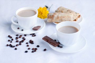 Two cup of coffee with milk, pancakes with jam and milk chocolate. Morning breakfast for two.