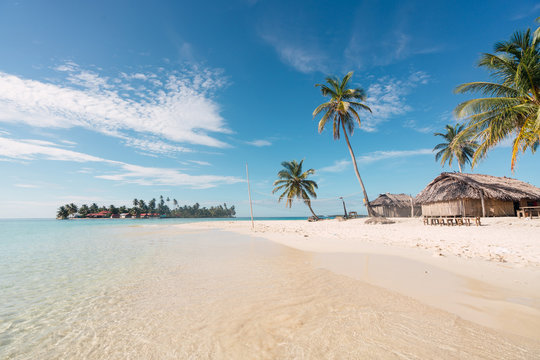 Sand beach with palms and building near water surface