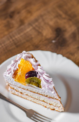 Slice of layered Birthday cake with cream with fruit in a plate on wooden table