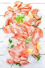 Shrimp with ice and lemon. Seafood. On a white wooden background. Top view. Free copy space.