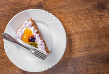 Slice of layered Birthday cake with cream with fruit in a plate on wooden table