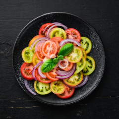 Salad of fresh tomatoes and onion in a black plate. On the old background. Top view. Free space for your text.
