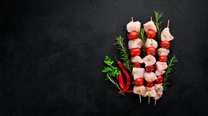 Raw chicken shish kebab with cherry tomatoes. Barbecue. On a black stone background. Top view. Free copy space.