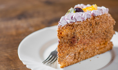 Slice of layered Birthday cake with cream with fruit in a plate on wooden table