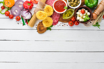 Ingredients for cooking pasta. Dry pasta. Mushrooms, sausages, tomatoes, vegetables. Top view. On a white wooden background. Free copy space.