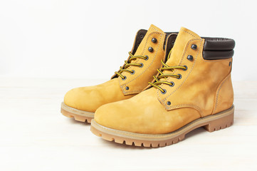 Yellow men's work boots from natural nubuck leather on wooden white background. Trendy casual...