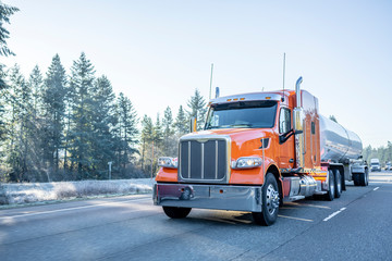 Orange big rig semi truck with long tank semi trailer transporting liquid and liquefied chemical...