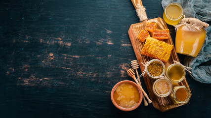 A set of honey and bee products. Honey in honeycomb. On a black wooden background. Free space for text. Top view.