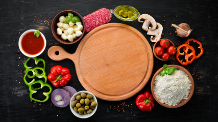 Ingredients for pizza. Mushrooms, sausages, tomatoes, vegetables. Top view. On a black wooden background. Free copy space.