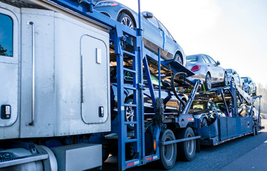 White big rig car hauler long distance semi truck transporting cars on two level semi trailer on the straight road