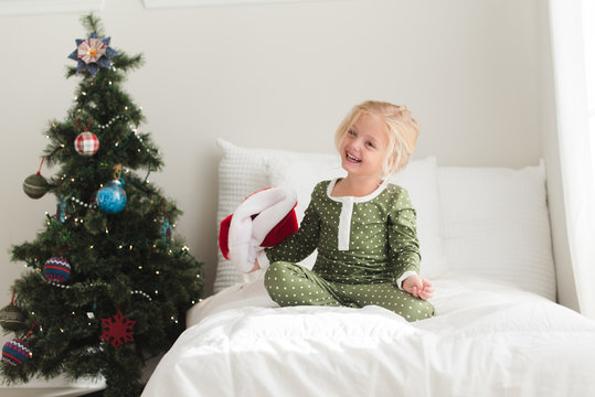 Young girl sitting on bed nearby a Christmas tree