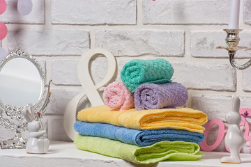 Multi-colored terry towels. Yellow green blue and purple cotton towels. Textiles on a white brick wall background. Rolled and folded towels on the table. © Yashkin Ilya