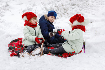 Children are sitting on a plaid and drinking tea in winter.