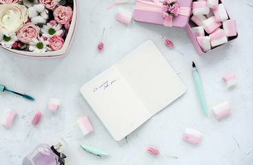 Open notebook on white table with flowers and marshmallow.Pastel colors.Flat lay.Overhead view.