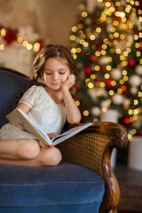 Little cute girl reads a book near christmas tree