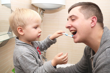 Dad and son brush their teeth in the bathroom. Father Brushing Teeth to Child