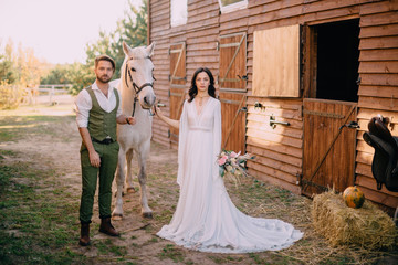 boho-style newlyweds standing near horse on ranch
