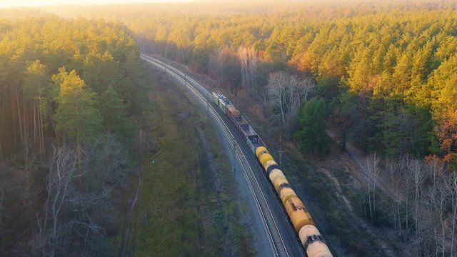 Freight train moves through the autumn forest at sunset. Aerial following shot