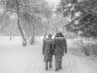 A black and white aged retro photo of two elderly men are walking along a path in a snowy park in winter