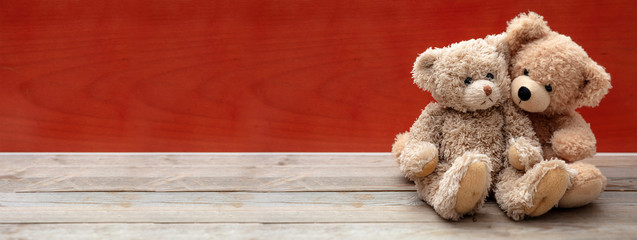 Love, friendship concept, tight hug. Teddy bears couple on wooden floor, red wall background, banner.