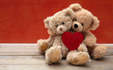 Love, friendship concept, tight hug. Teddy bears couple on wooden floor, red wall background