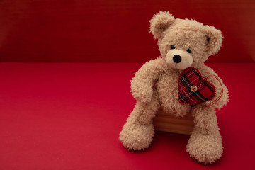 Valentines day. Teddy bear with a fabric heart against red background, copy space