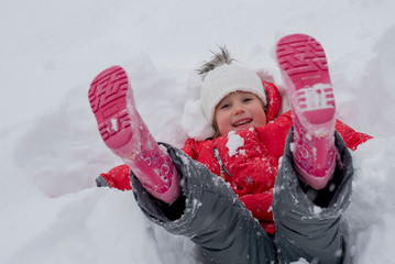 Little girl lying on his back in the snow and having fun 