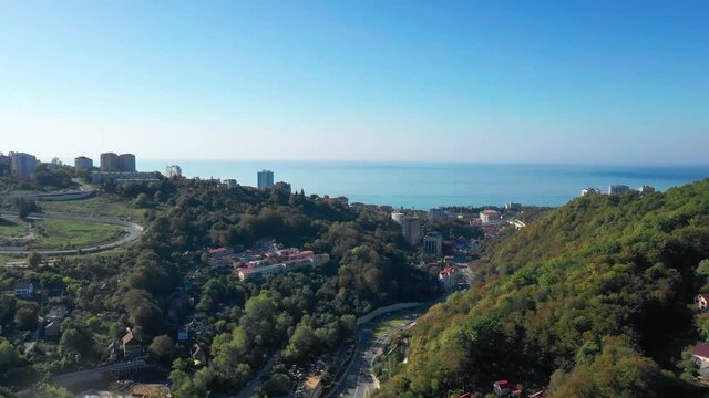 Aerial photography of the road on which cars go to the sea. The holiday season in Sochi. Hot summer. Stay at the resort. Mountains, sea, road. Travelling by car.