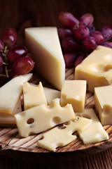 Pieces of cheese and bunches of grapes on wood illuminated with selective light