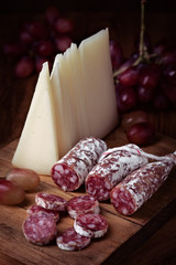 Spanish cheese and fuet on wooden board, dim light