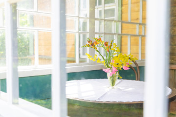 Yellow-pink bouquet of wild flowers on the table. Photo in bright colors. Table and bouquet can be seen through the window of the balcony or veranda.