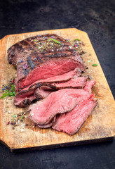 Traditional barbecue dry aged sliced roast beef steak with herbs as closeup on an old cutting board © HLPhoto