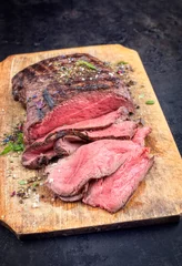Foto op Canvas Traditional barbecue dry aged sliced roast beef steak with herbs as closeup on an old cutting board © HLPhoto