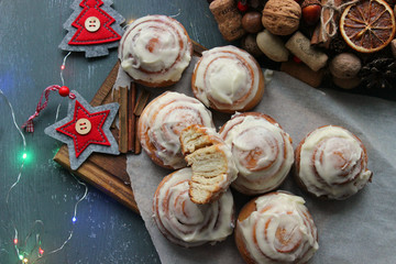 Cinnamon rolls for Christmas. Christmas cakes. Buns in glaze on a wooden table, scattered nuts and cinnamon sticks, rustic style. Homemade cake. Christmas background. Greeting card.