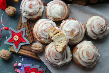 Cinnamon rolls for Christmas. Christmas cakes. Buns in glaze on a wooden table, scattered nuts and cinnamon sticks, rustic style. Homemade cake. Christmas background. Greeting card.