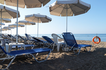 A sea resort with sun loungers and umbrellas on sandy beach on summer sunny day; The concept of comfort place for family vacations or holidays; Sandy beach on the coast