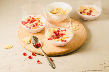 Homemade yogurt with garnet grains and flakes in glass/Homemade yogurt with garnet grains and flakes in glass on a wooden tray and white stone table. Selective focus